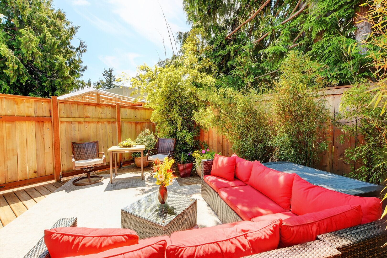 Un jardin avec un canapé rouge, des fauteuils en osier, une petite table et un jacuzzi.