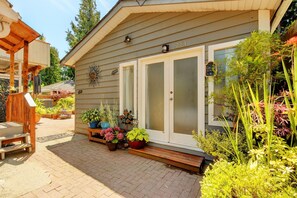 A house with a covered porch, a front door with frosted glass panels, and a variety of potted plants and flowers in front.