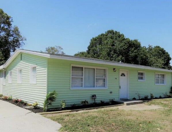 Uma casa móvel térrea, de cor verde clara, com varanda frontal, um pequeno jardim e caixa de correio.