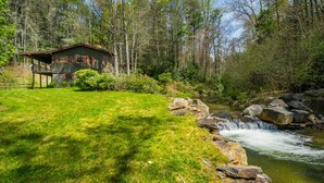 A cabin with a porch, surrounded by a grassy yard and a small waterfall. - Private Riverfront Cabin: 9 Acres,  Trails to Waterfalls (Sapphire)