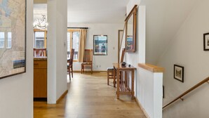 A hallway with wooden flooring, a dining area with chairs and a table, and a staircase with a wooden handrail.