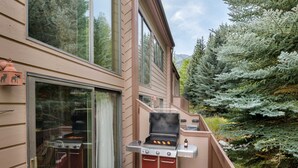 An outdoor grill area with a sliding glass door, a wooden deck, and a view of trees and mountains.