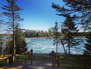 A wooden deck leading to a river with a view of the water and surrounding trees.
