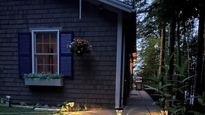 A house with a brick exterior, a window with shutters, and a pathway leading to the entrance. - Oceanfront Maine Acadia Cottage (Hancock)