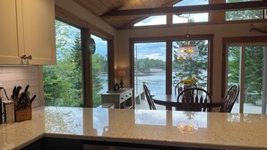 A kitchen with a view of a river, wooden ceiling beams, and a dining area with a table and chairs. - Oceanfront Maine Acadia Cottage (Hancock)