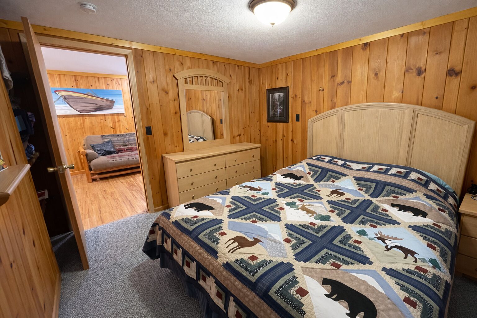 Un dormitorio con un revestimiento de madera, una cama con colcha estampada, un aparador y un espejo.