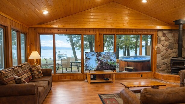 Un interior de cabaña acogedor con techo de madera, ventanas amplias, chimenea y televisor.