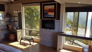Una sala de estar moderna con un ventanal grande, un televisor de pantalla plana montado en una pared blanca y una mesa de centro de vidrio.