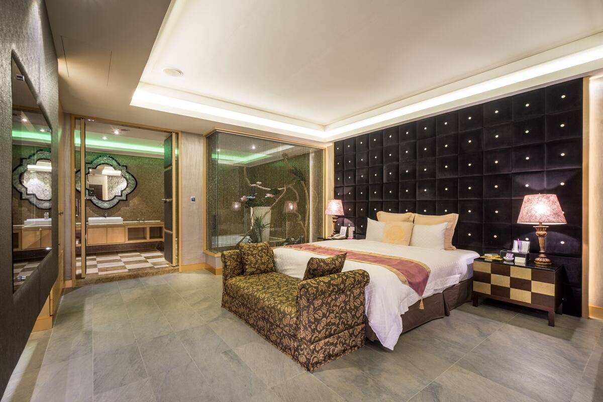 Een moderne hotelkamer met een groot bed, een slaapbank, een nachtkastje en een badkamer met glazen wanden.