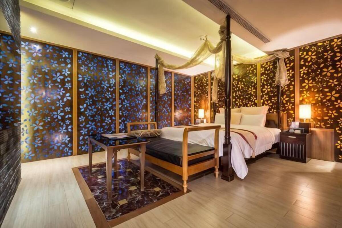 Een hemelbed met een baldakijn, een nachtkastje en een wand met een bloemenpatroon.