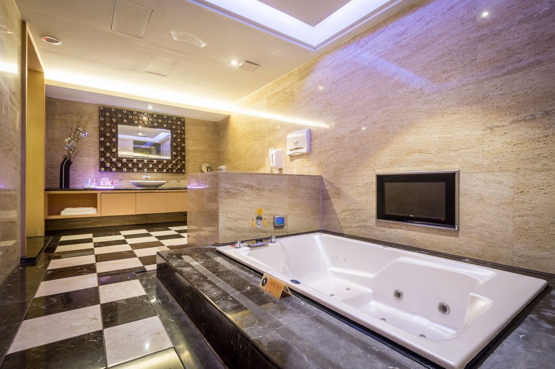 Ein modernes Badezimmer mit einer großen Badewanne, einem Schachbrettfußboden, einem Waschtisch mit Spiegel und einem an der Wand montierten Fernseher.