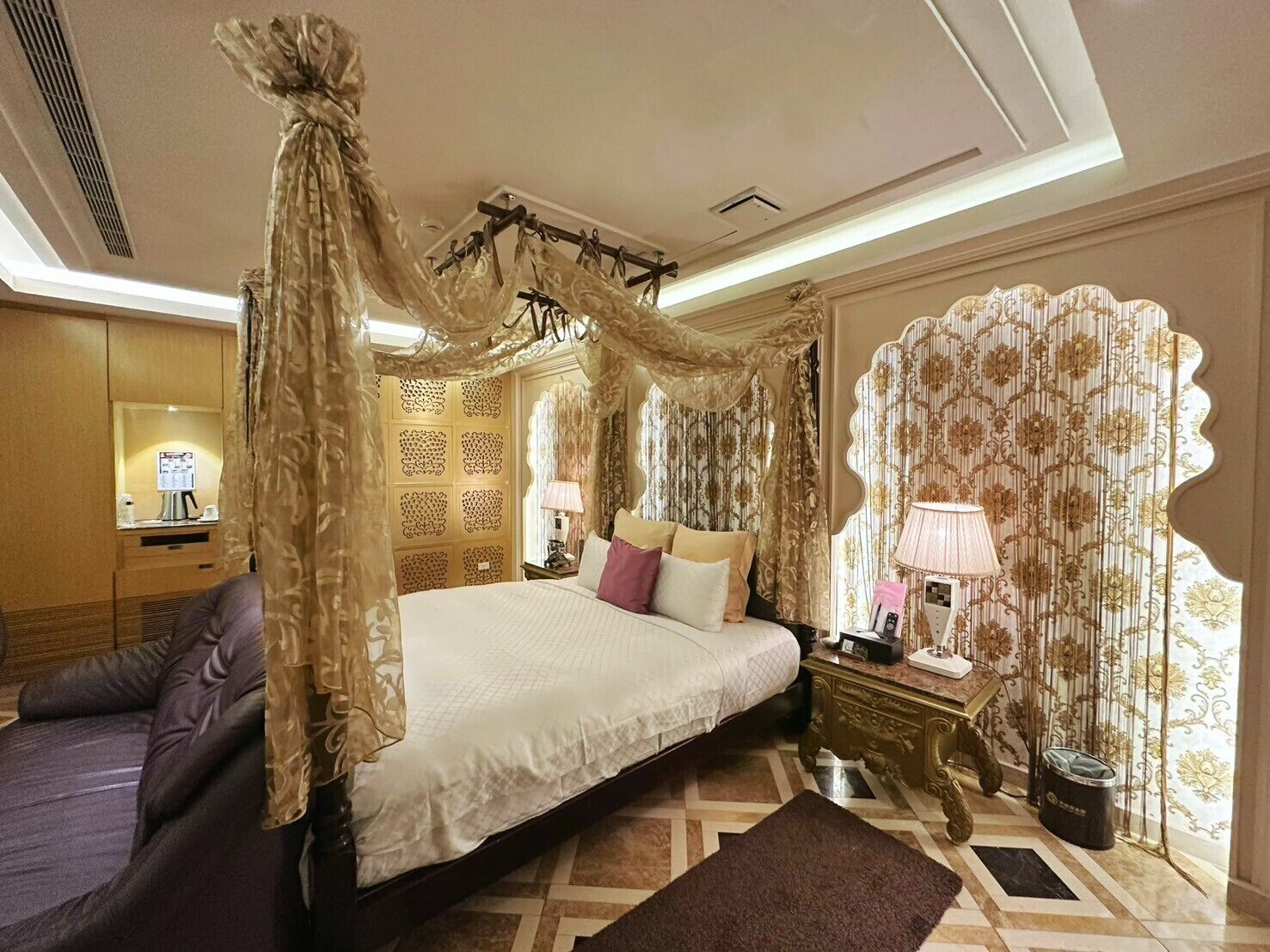 Um quarto luxuoso com cama de dossel, um espaço de estar com sofá e um painel decorativo na parede.