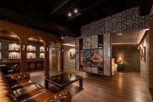A modern lounge area with a bar, leather seating, and a large TV screen.