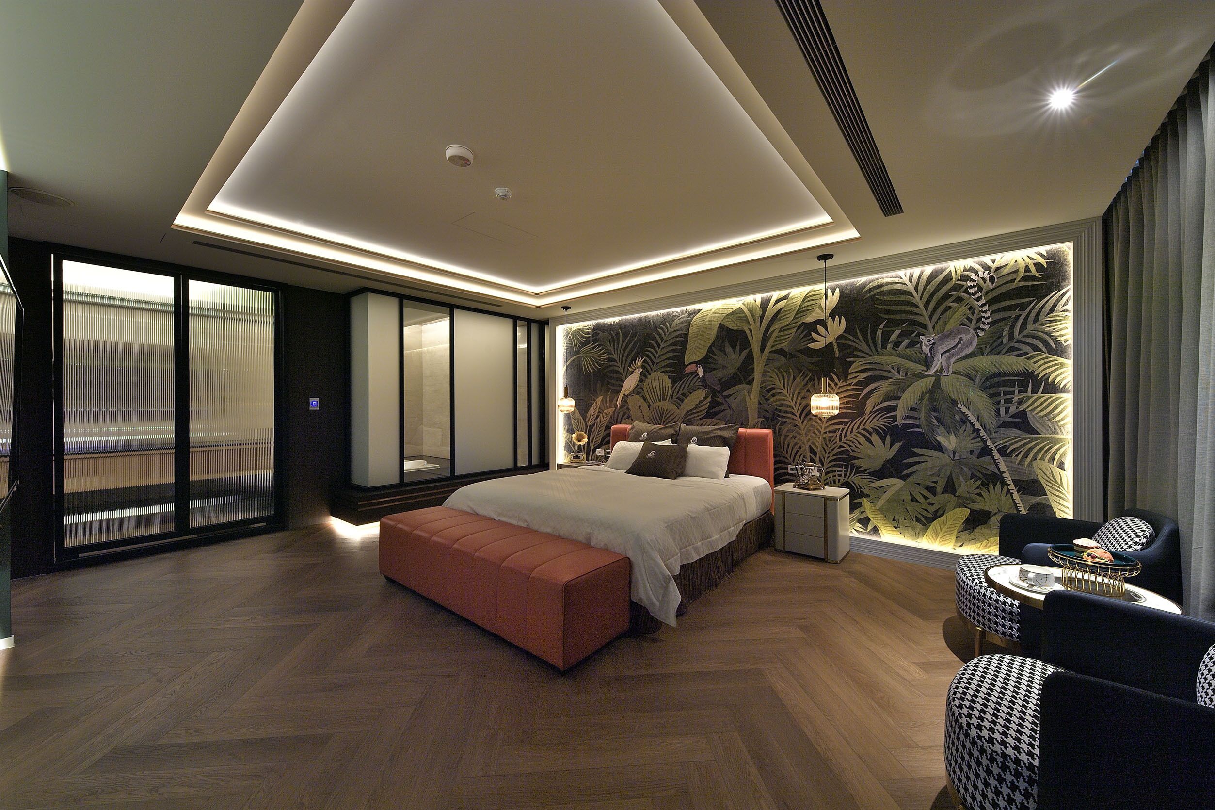 A modern bedroom with a large bed, a bench, a nightstand, and a seating area with a table.