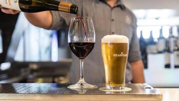 Una persona versa vino rosso in un bicchiere e una birra con l'etichetta 'HEADSTART' su un bancone da bar.
