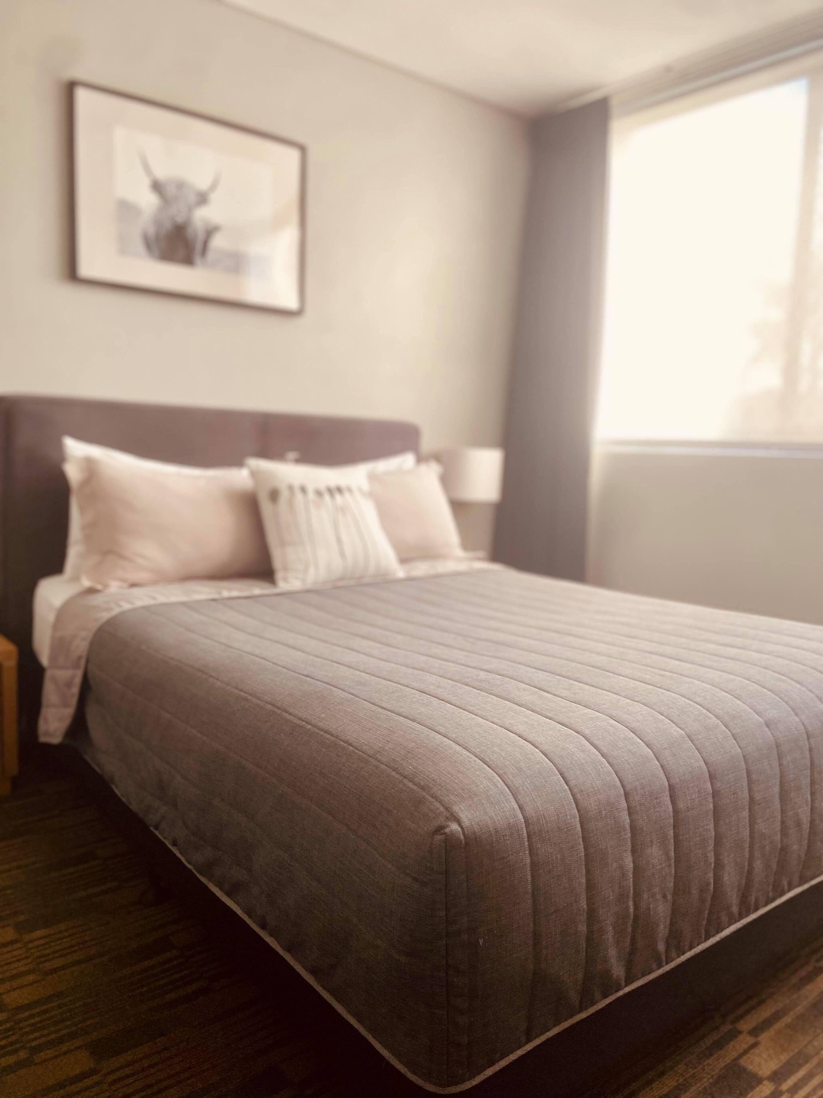 A neatly made bed with a striped bedspread, a headboard, and a nightstand with a lamp.