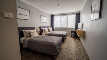 A hotel room with two beds, a large window with curtains, a wall-mounted lamp, and framed artwork.