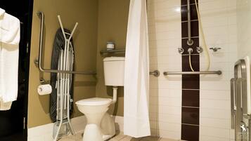 Une salle de bain équipée de toilettes, de barres d’appui, d’un rideau de douche et d’un porte-serviettes.