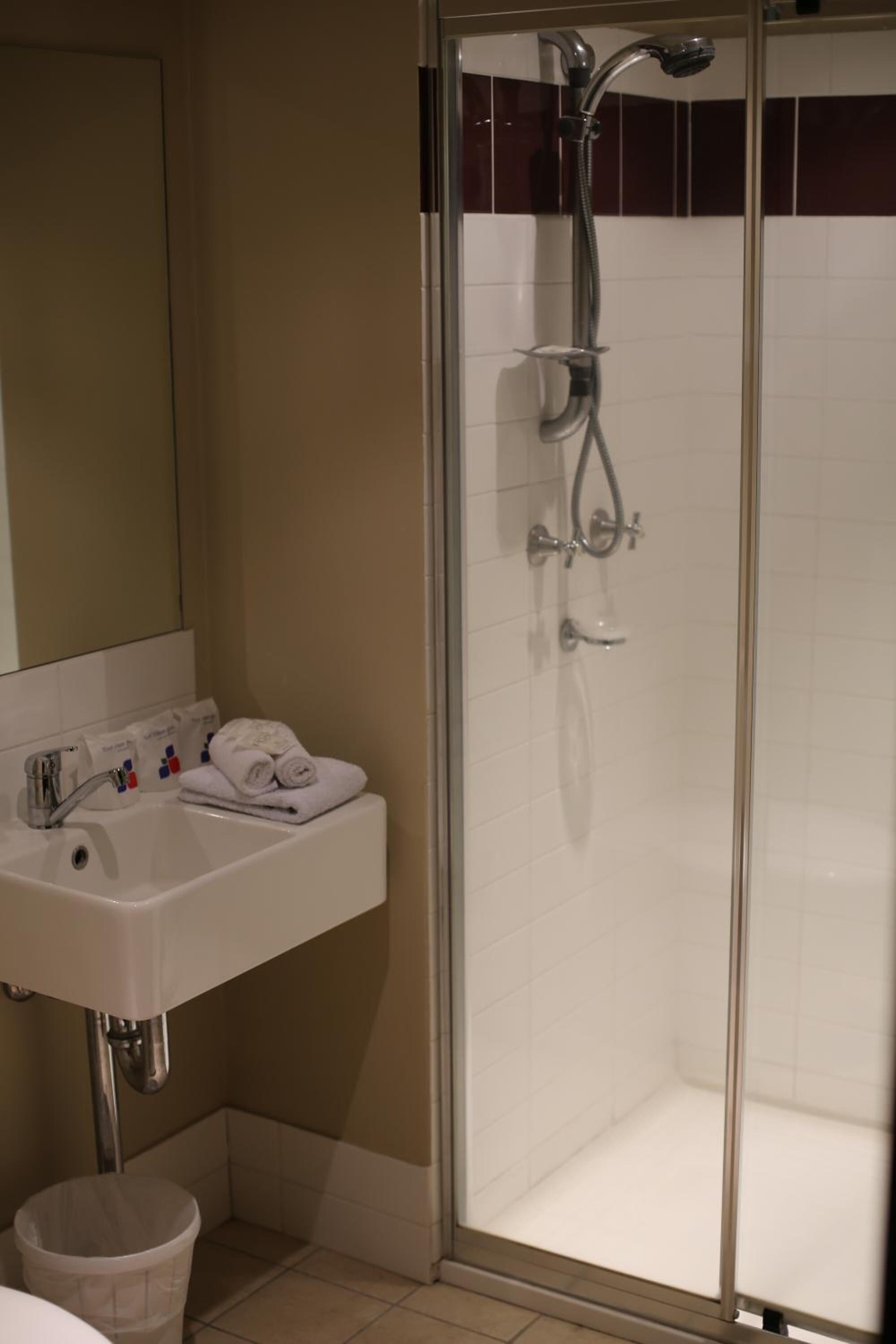 Un bagno con doccia vetro, lavandino bianco e specchio.
