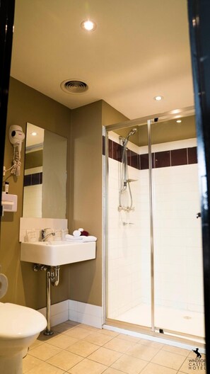 Un baño con ducha envuelta en vidrio, lavamanos con artículos de aseo y secador de pelo en la pared.