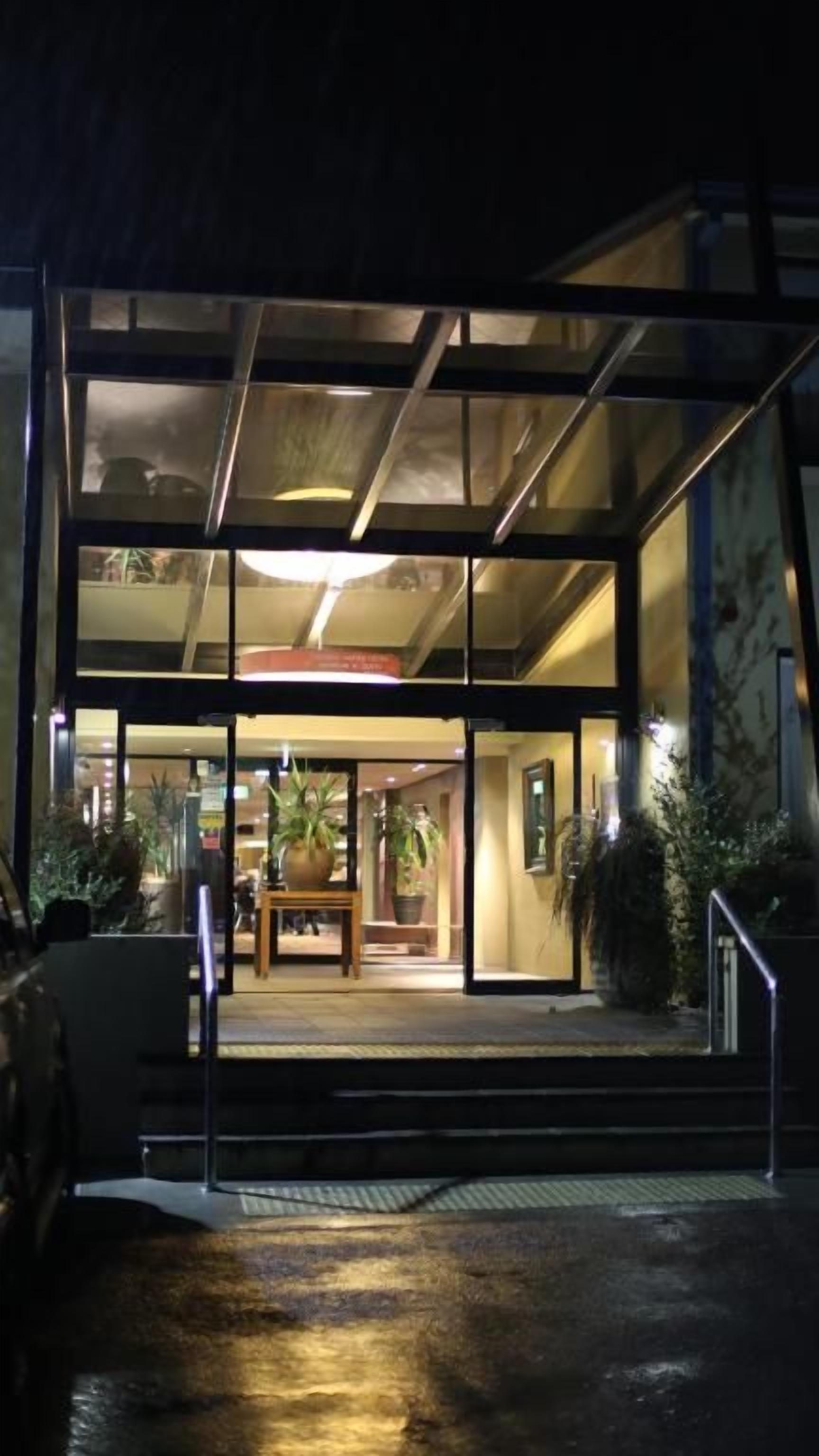 Una entrada moderna de edificio con puertas de vidrio, una escalera y plantas de interior.