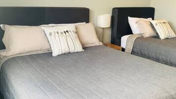 Dos camas con ropa de cama gris, una mesita de noche con lámpara y cuadros en las paredes.