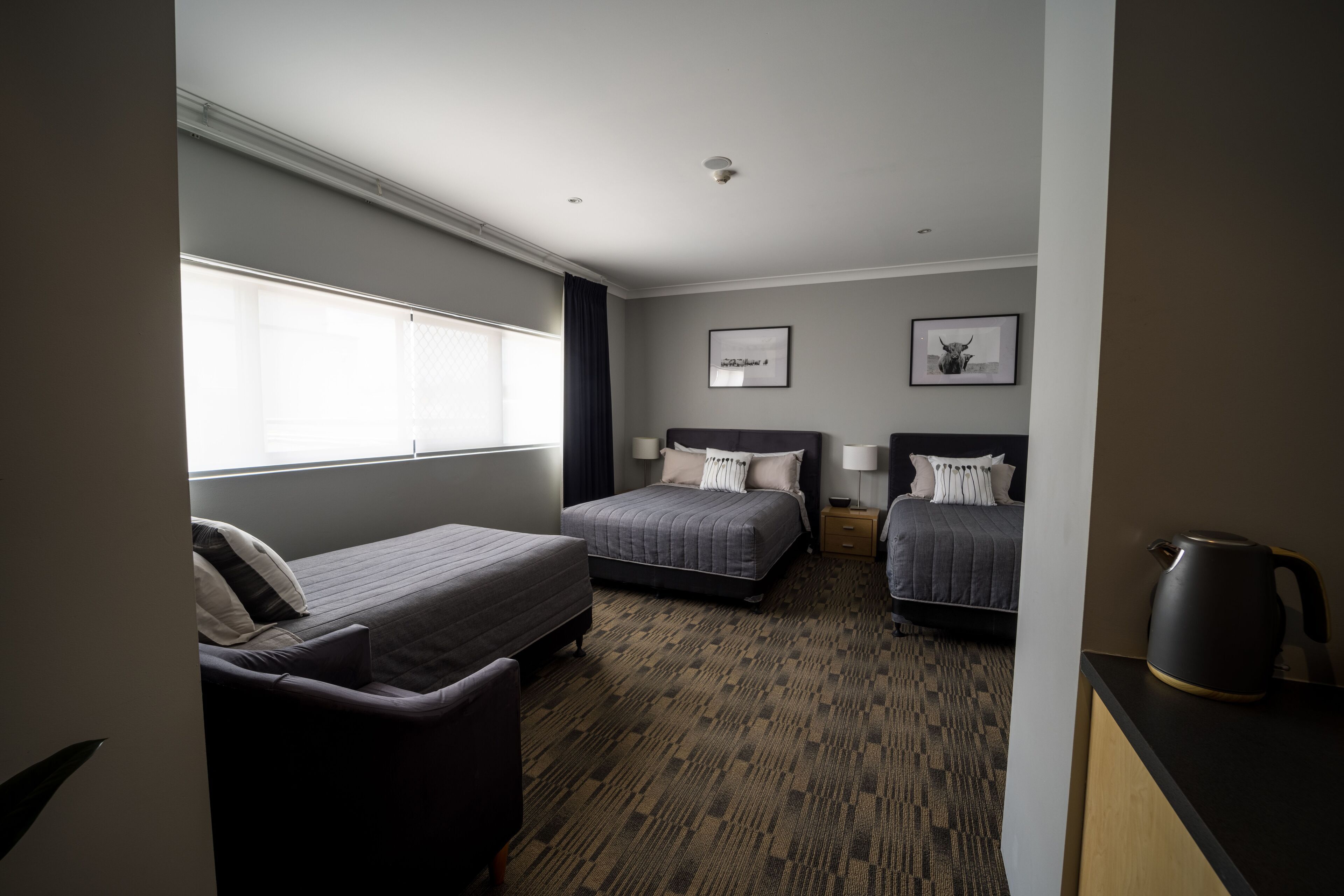 A hotel room with two beds, a sofa, a coffee maker, and a window with blinds.