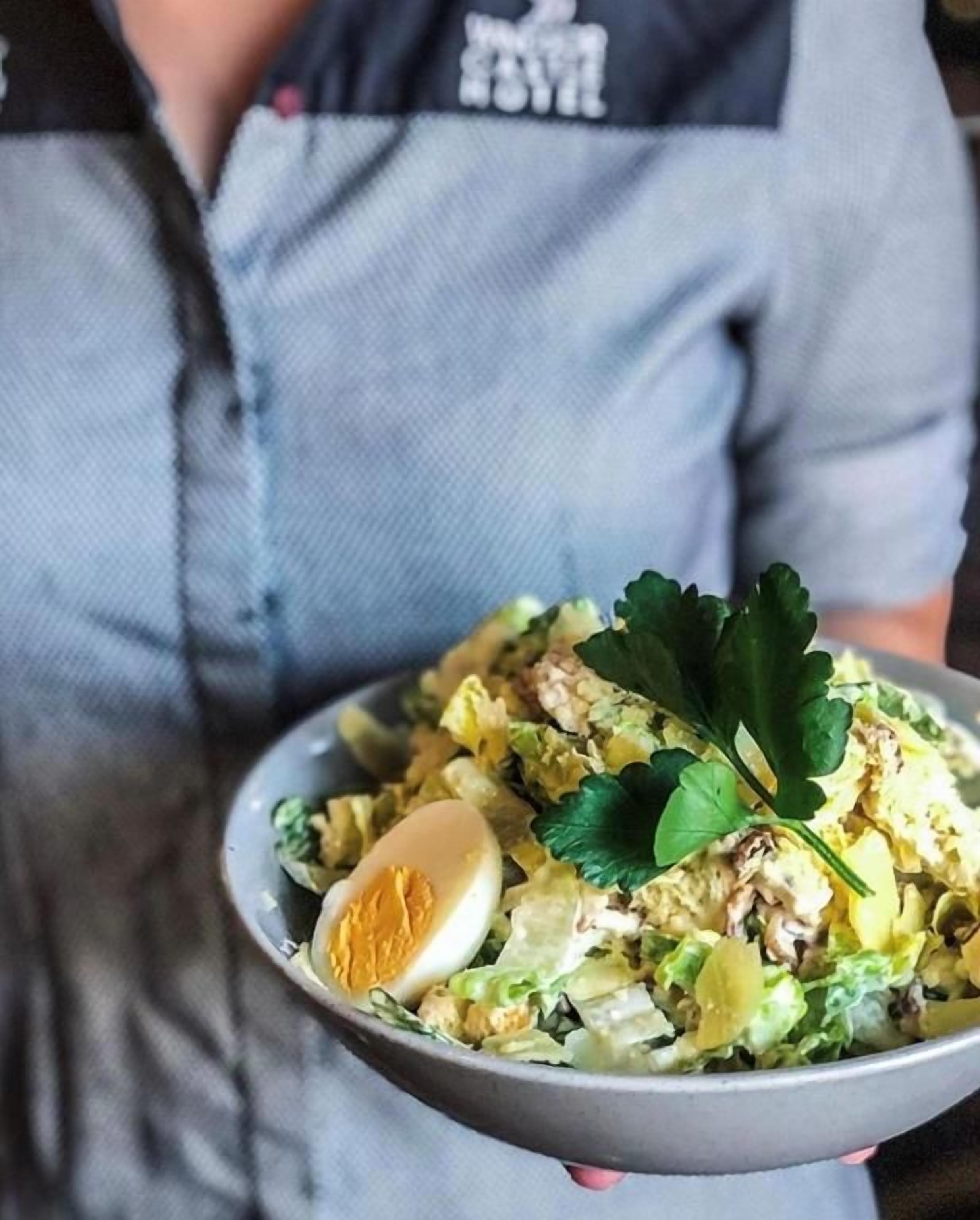 A person holding a bowl of salad with a boiled egg and greens.