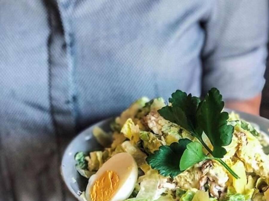 A person holding a bowl of salad with a boiled egg and greens.
