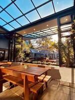 Un área de comedor al aire libre con mesas y bancos de madera, techo de vidrio y vista a un edificio que dice 'THE CASTLE'.