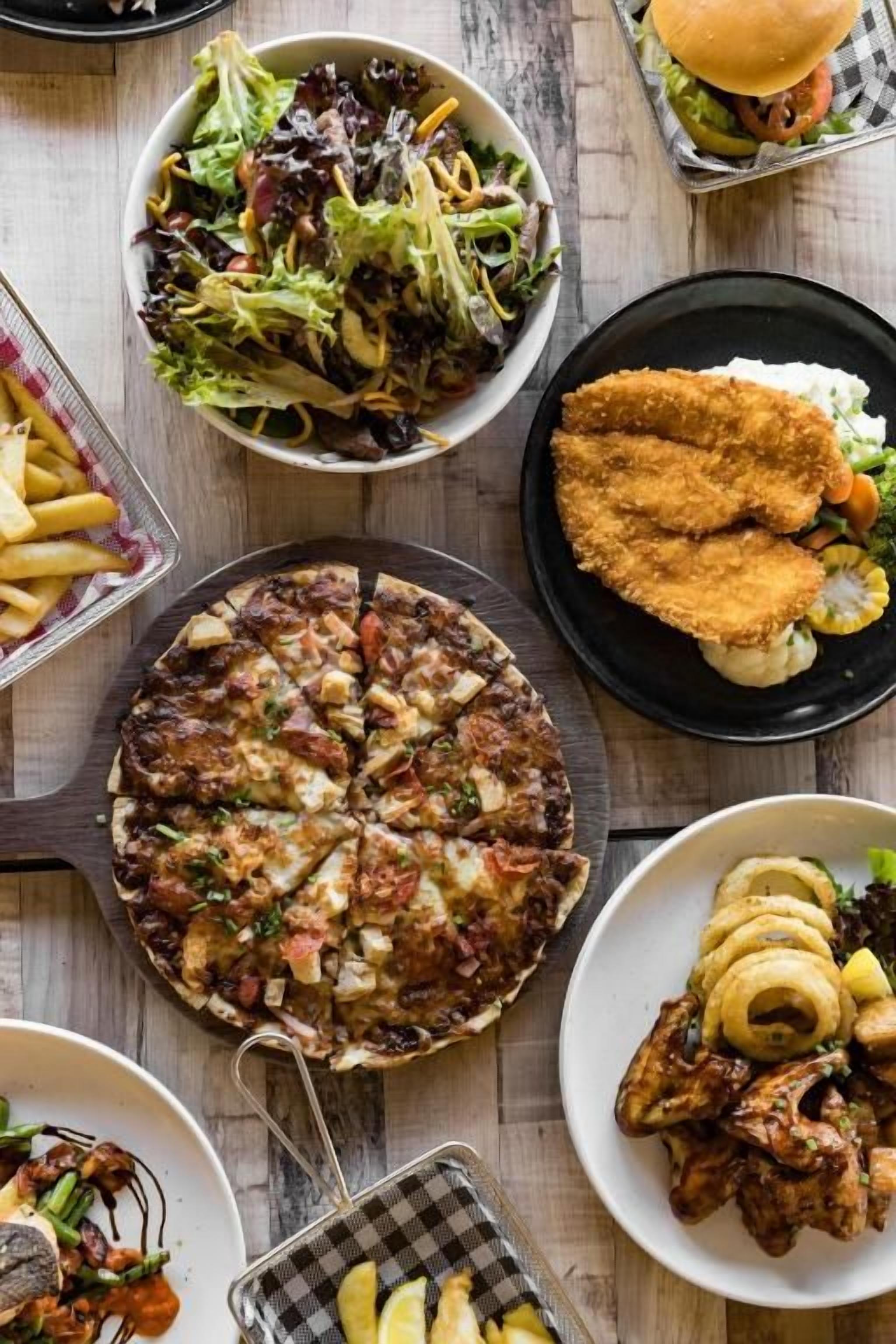 A variety of dishes including a salad, a pizza, and fried items on a wooden table.