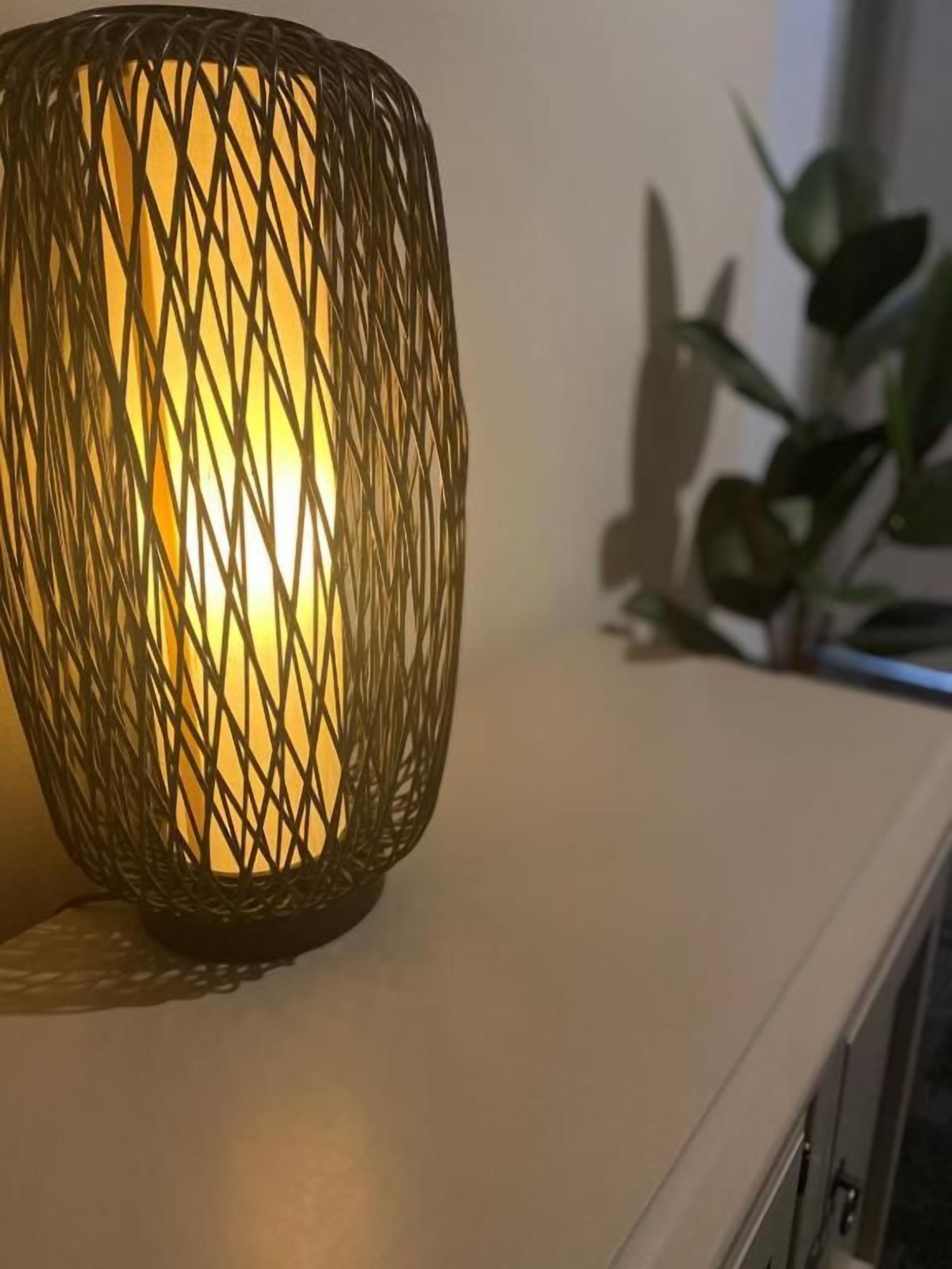 Una vela encendida en un soporte tejido sobre una superficie blanca.