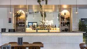 Zona de bar con una barra alargada, diversas opciones de asiento y una variedad de botellas y vasos.