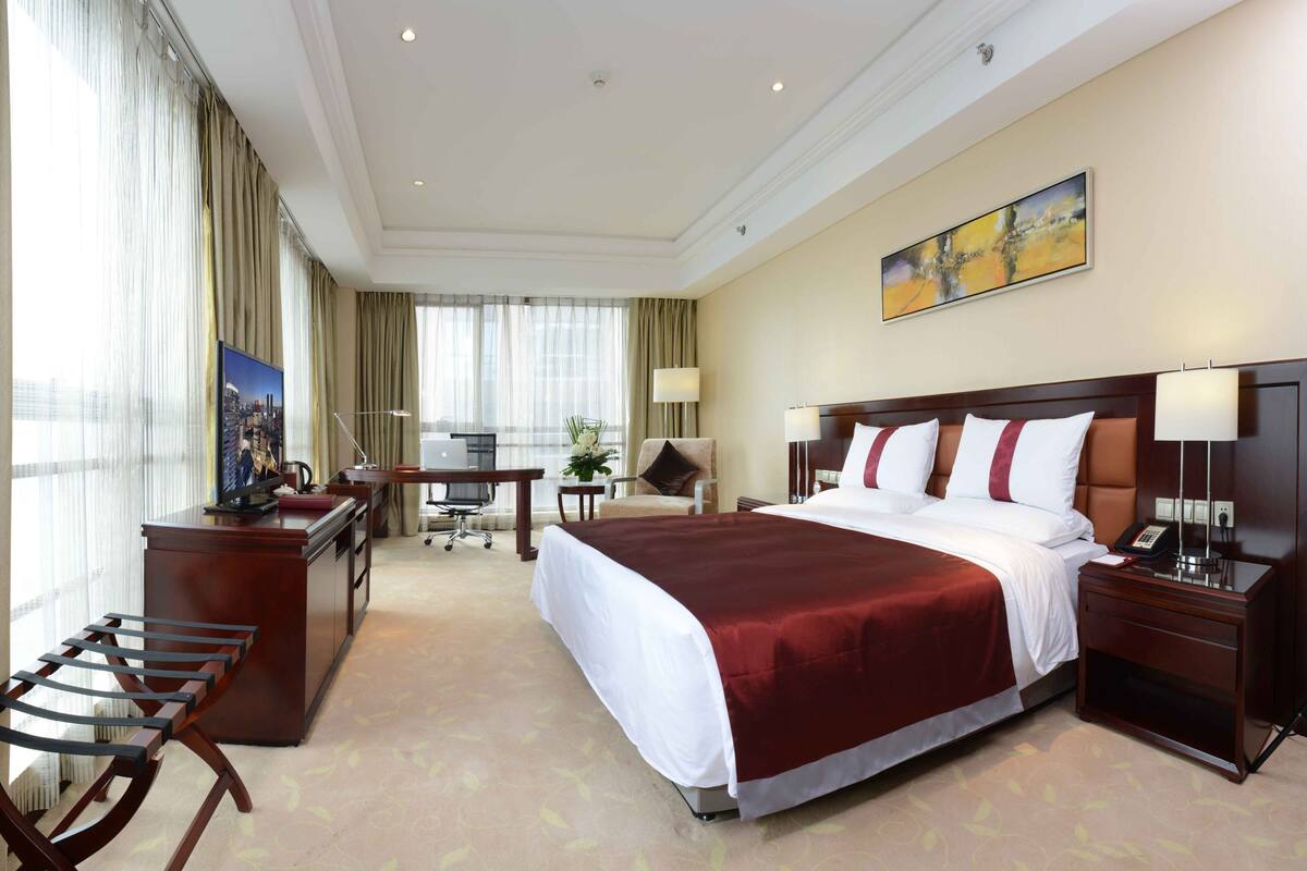 Ein Hotelzimmer mit einem großen Bett, einem Schreibtisch, einem Sessel und einem Fernseher.