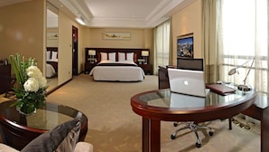 Une chambre d’hôtel comprenant un lit, un bureau avec un ordinateur portable, une chaise, une petite table ronde en verre, un miroir, une télévision et une fenêtre avec des rideaux.
