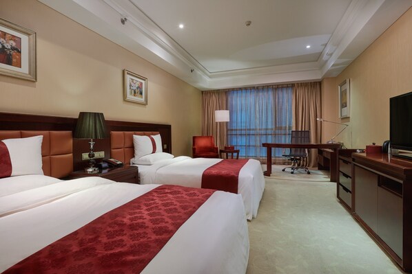 A hotel room with two beds, a desk, a chair, a TV, and a window with curtains.