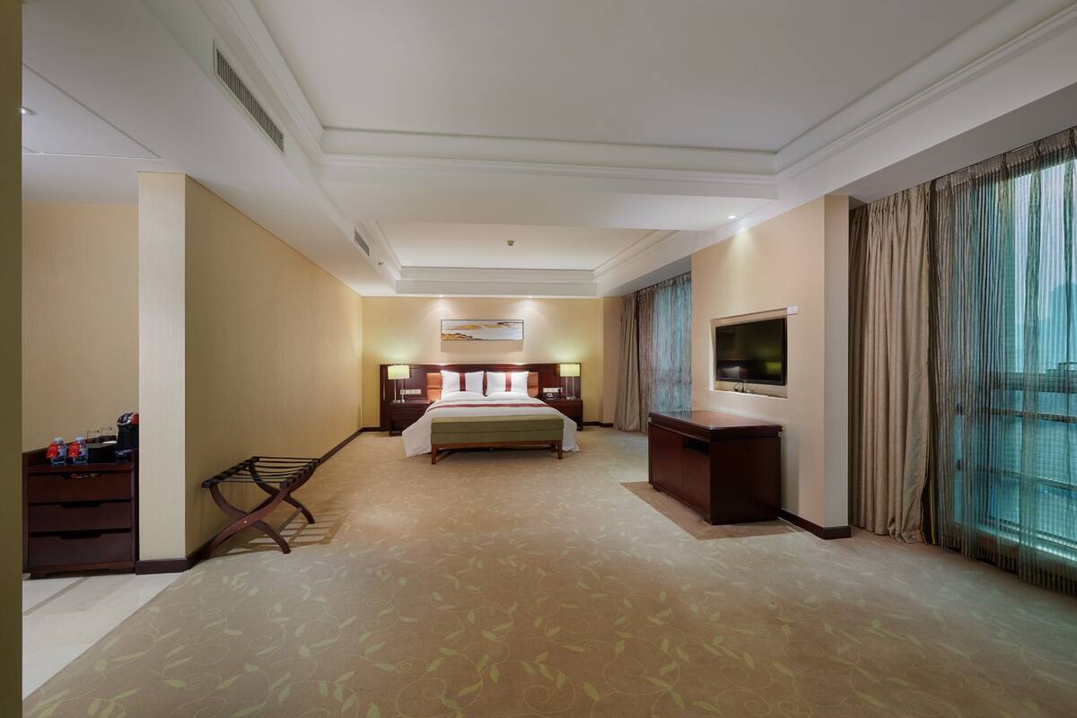 Ein Hotelzimmer mit einem großen Bett, Nachttischen, einem Fernseher und einem Fenster mit Vorhängen.
