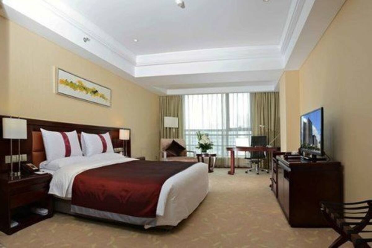 Ein Hotelzimmer mit einem großen Bett, einem Schreibtisch, einem Fernseher und einem Fenster mit Vorhängen.