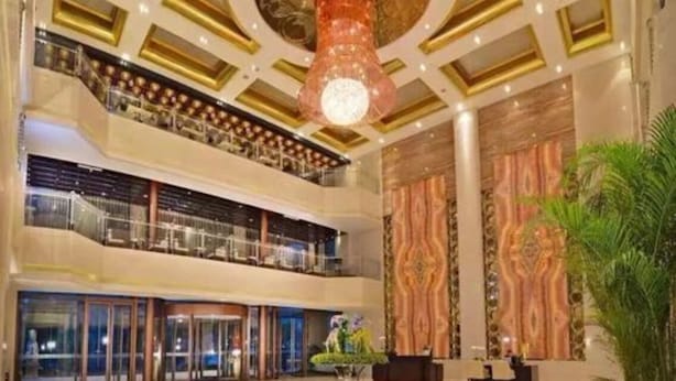 Un hall d’hôtel à plusieurs niveaux, agrémenté d’un imposant lustre, d’un comptoir d’accueil et d’une grande plante.