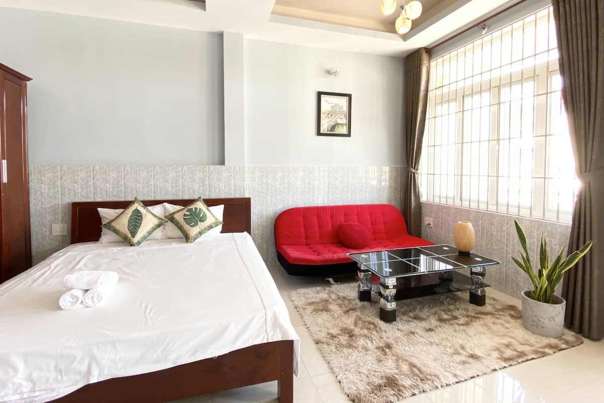 A hotel room with a bed, a red sofa, a glass coffee table, and a potted plant.