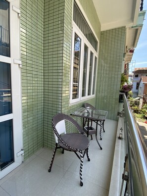 A balcony with green tiled walls, a glass table, and two wicker chairs. - Hue Lovely Homestay  (Hue)