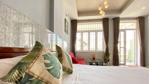 Una habitación de hotel con una cama grande, una mesita con un florero y una ventana con cortinas.
