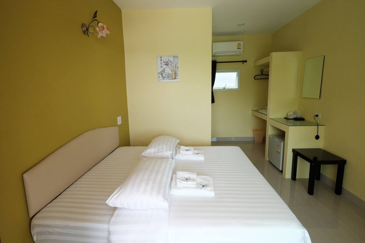 A hotel room with a large bed, a small desk, a mirror, and a wall-mounted air conditioner.