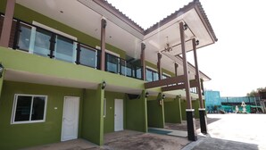 Un edificio de dos pisos con fachada verde, ventanas amplias y un espacio exterior cubierto con techo.