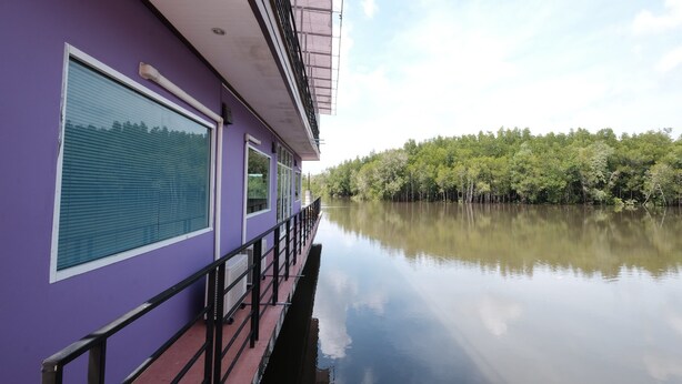 Un edificio morado con amplios ventanales y barandilla que da a un río tranquilo.