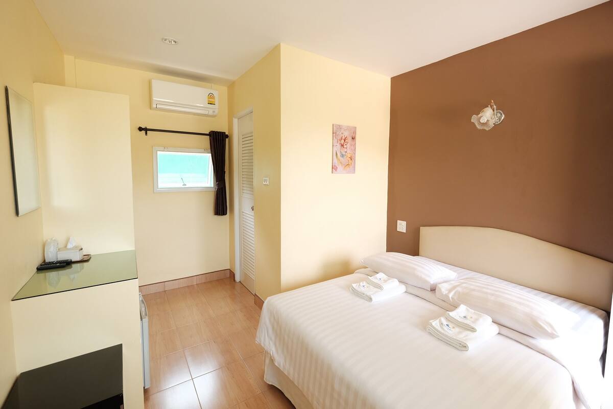 A hotel room with a bed, a desk, a mirror, an air conditioner, and a window.