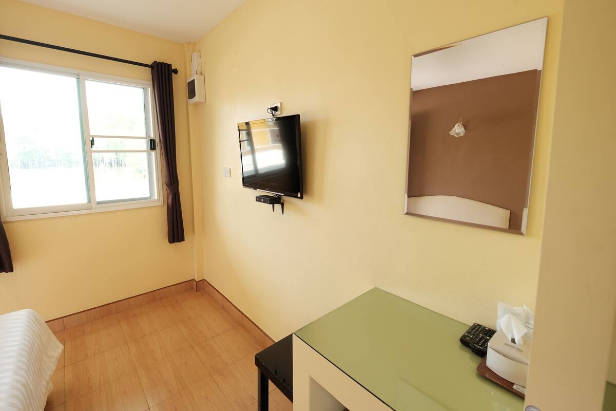 A hotel room with a bed, a desk with a computer, a TV, and a window with curtains.