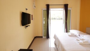 Habitación de hotel con cama, televisor de pantalla plana montado en la pared y puerta corredera que da a un balcón.