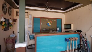 Un mostrador de recepción con una barra azul, un ventilador de techo y un cartel de Srikantala Resort.