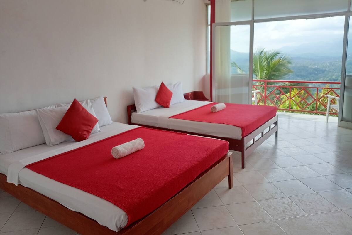 Habitación de hotel con dos camas, cada una con ropa de cama roja y blanca, y un balcón con barandilla roja.